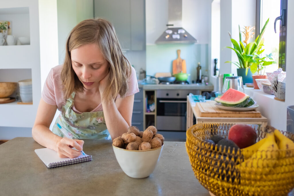 focused housewife planning weekly menu her kitchen writing down grocery list notebook cooking home concept
